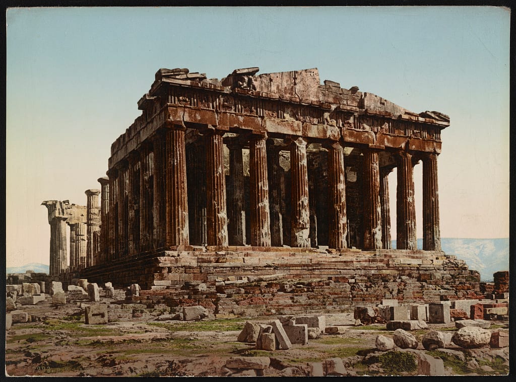 Colour print of the ruined Parthenon: rust-coloured columns and a broken roofline under a pale blue sky, fallen marble blocks in front