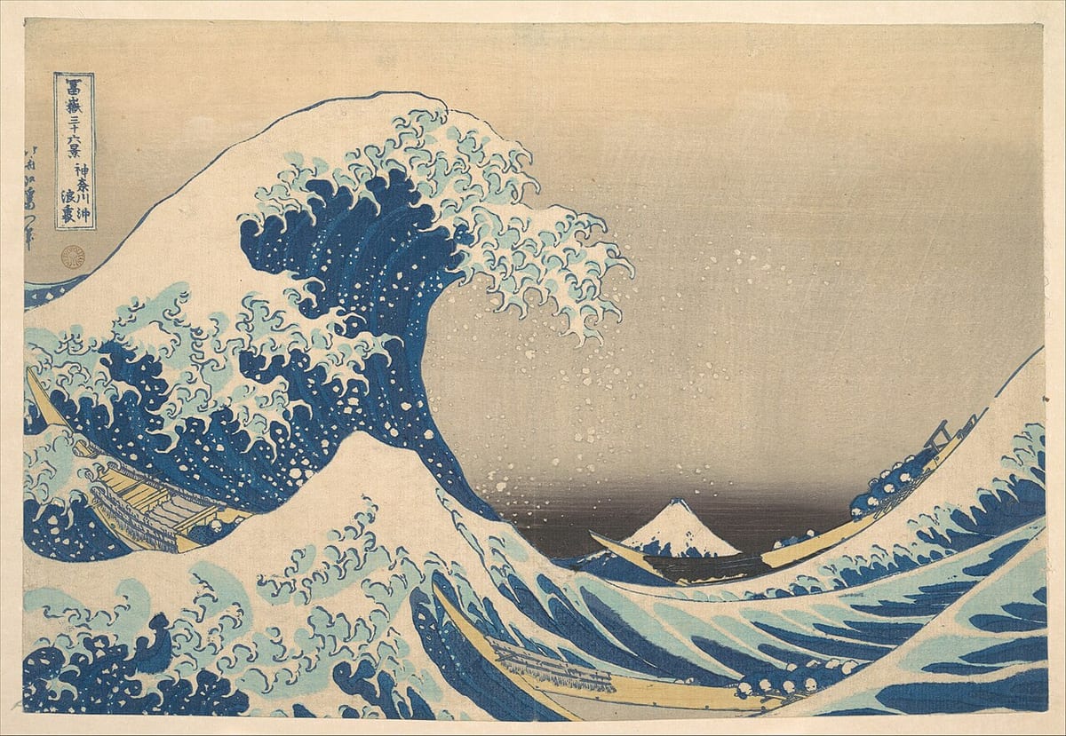 Woodblock print of a towering blue wave with claw-like white foam curling over narrow rowing boats, a small snow-capped Mount Fuji in the distance