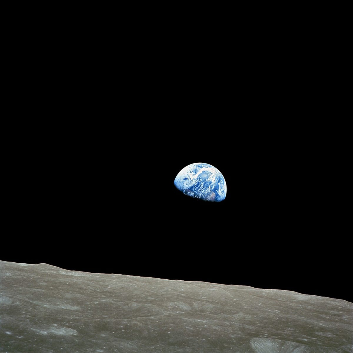 A half-lit blue and white Earth rising above the grey, cratered horizon of the Moon against black space