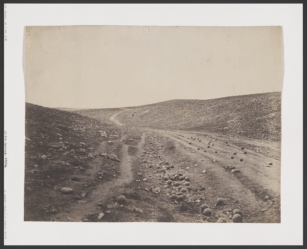 Sepia photo of a bare, rocky valley road strewn with cannonballs, low hills rising on either side under a blank sky